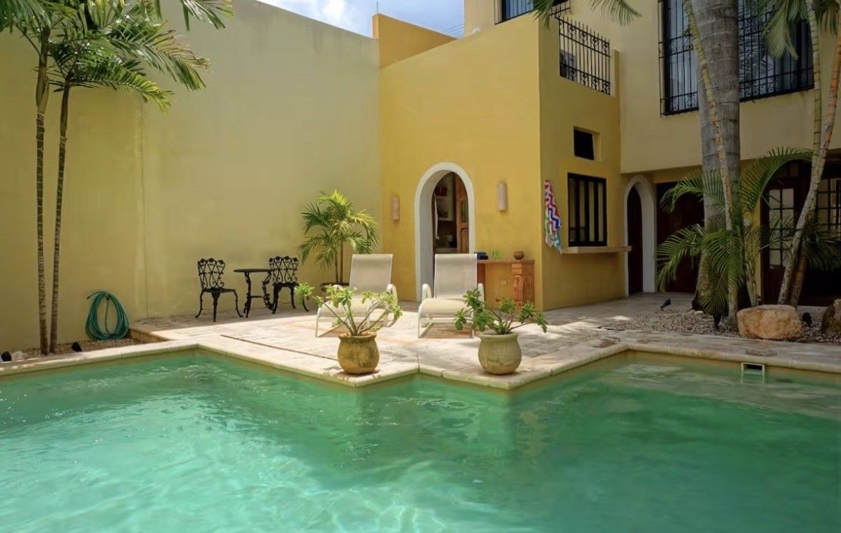 Mérida courtyard with palm trees, yellow walls, lounge chairs, and a swimming pool